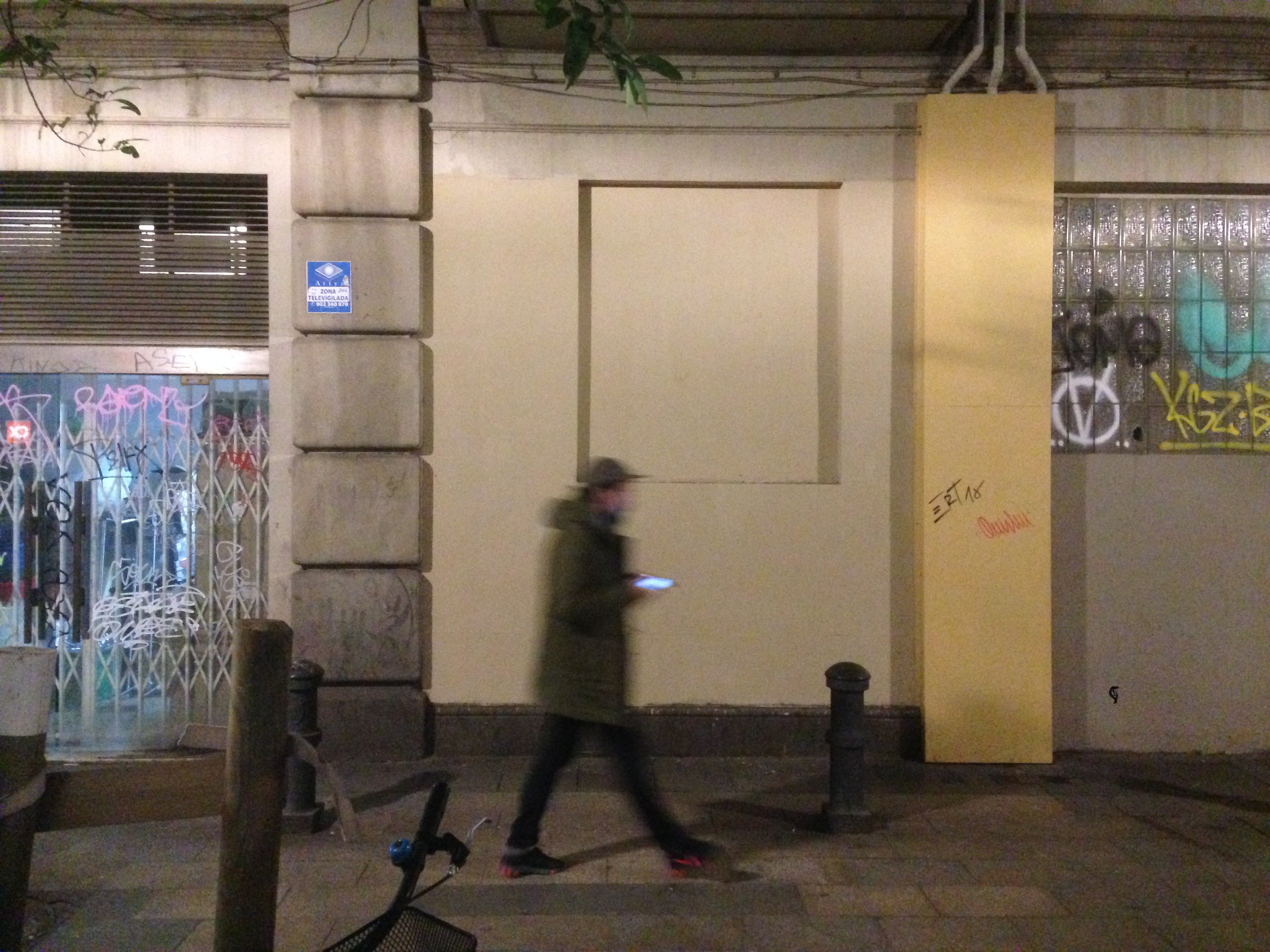 Un chico pasa, de noche, por la pared con el grafiti ya borrado.